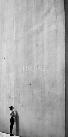 High Resolution: Individual with short hair wearing dark pants and light shirt standing against tall concrete wall casting shadow minimalistic composition download. | HRJPG.com