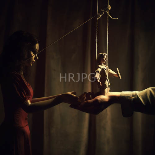 puppeteer hands craft marionette figure in crimson red velvet against black velvet drapes